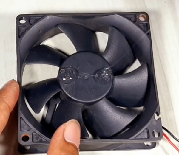 A glue gun applying glue to the center of the fan